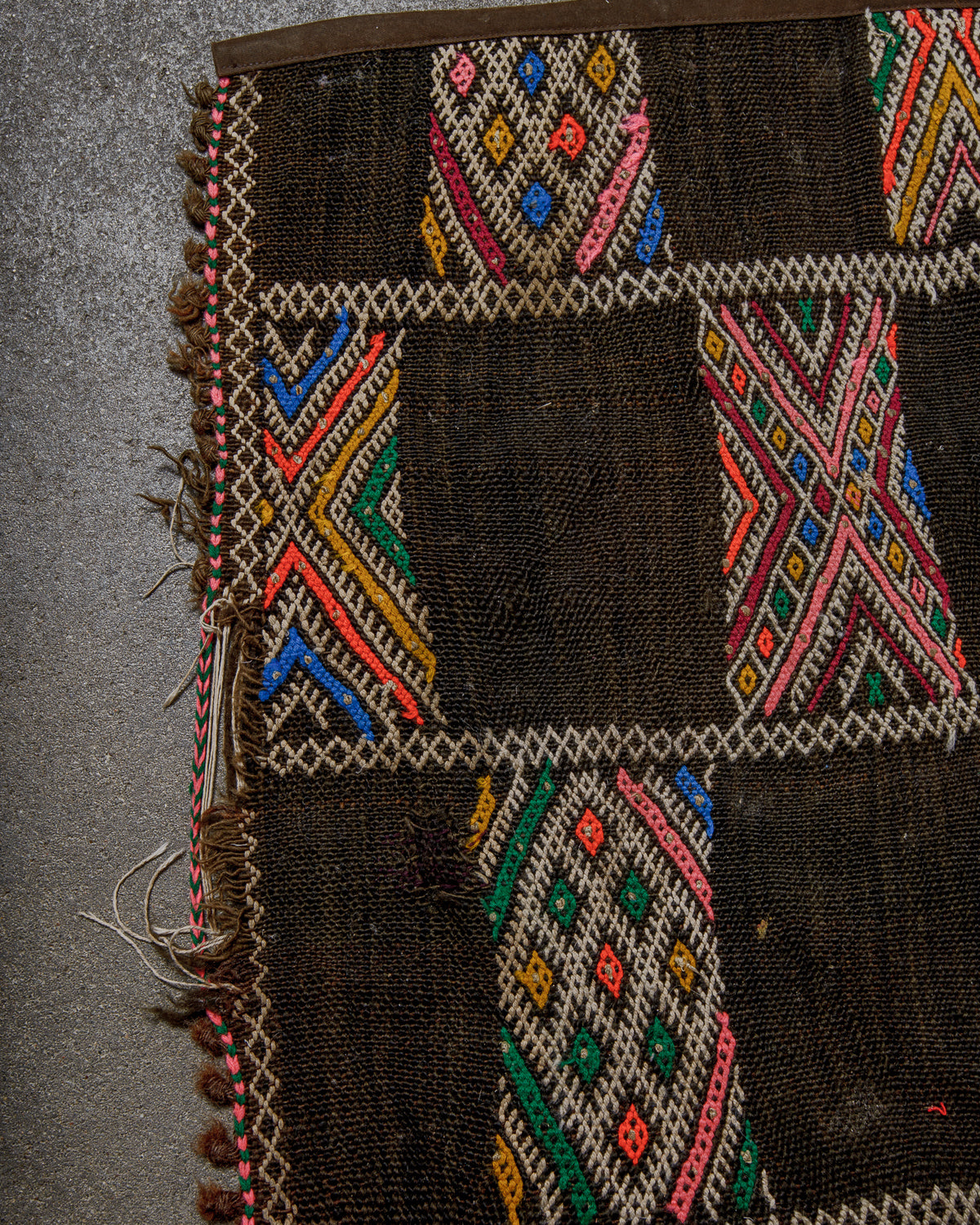 Close-up of a vintage kelim rug with colourful geometric patterns on a concrete background.